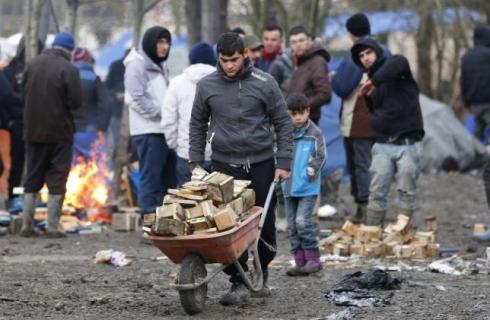 A migrant pushes a wheelbarrow in a muddy field at a camp of makeshift shelters called the Grande Synthe jungle, near Calais